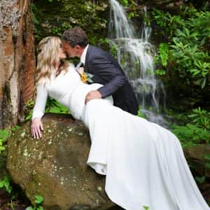 Groom leaning over his bride on a rock kissing her romantically at a waterfall in the Smoky Mountains
